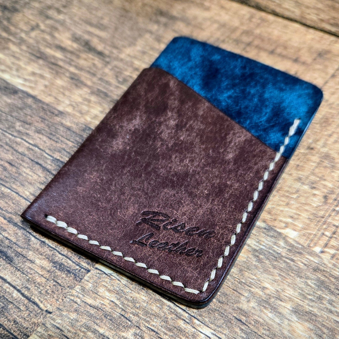 A handmade brown and blue full-grain leather cardholder with 'Risen Leather' branded on the side.