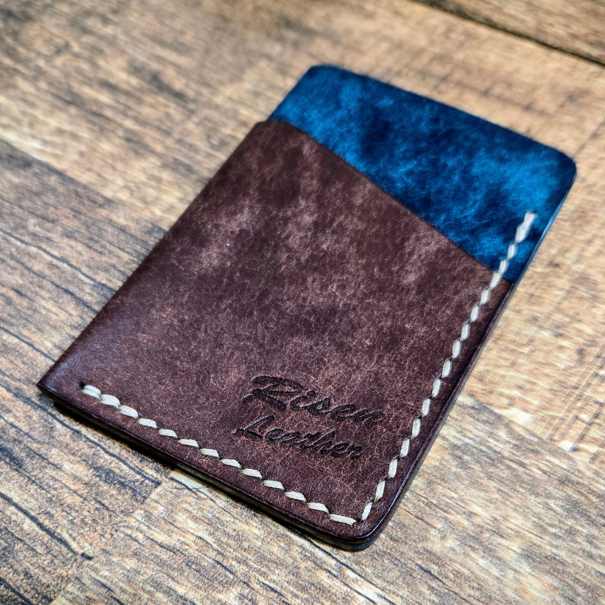 A handmade brown and blue full-grain leather cardholder with 'Risen Leather' branded on the side.