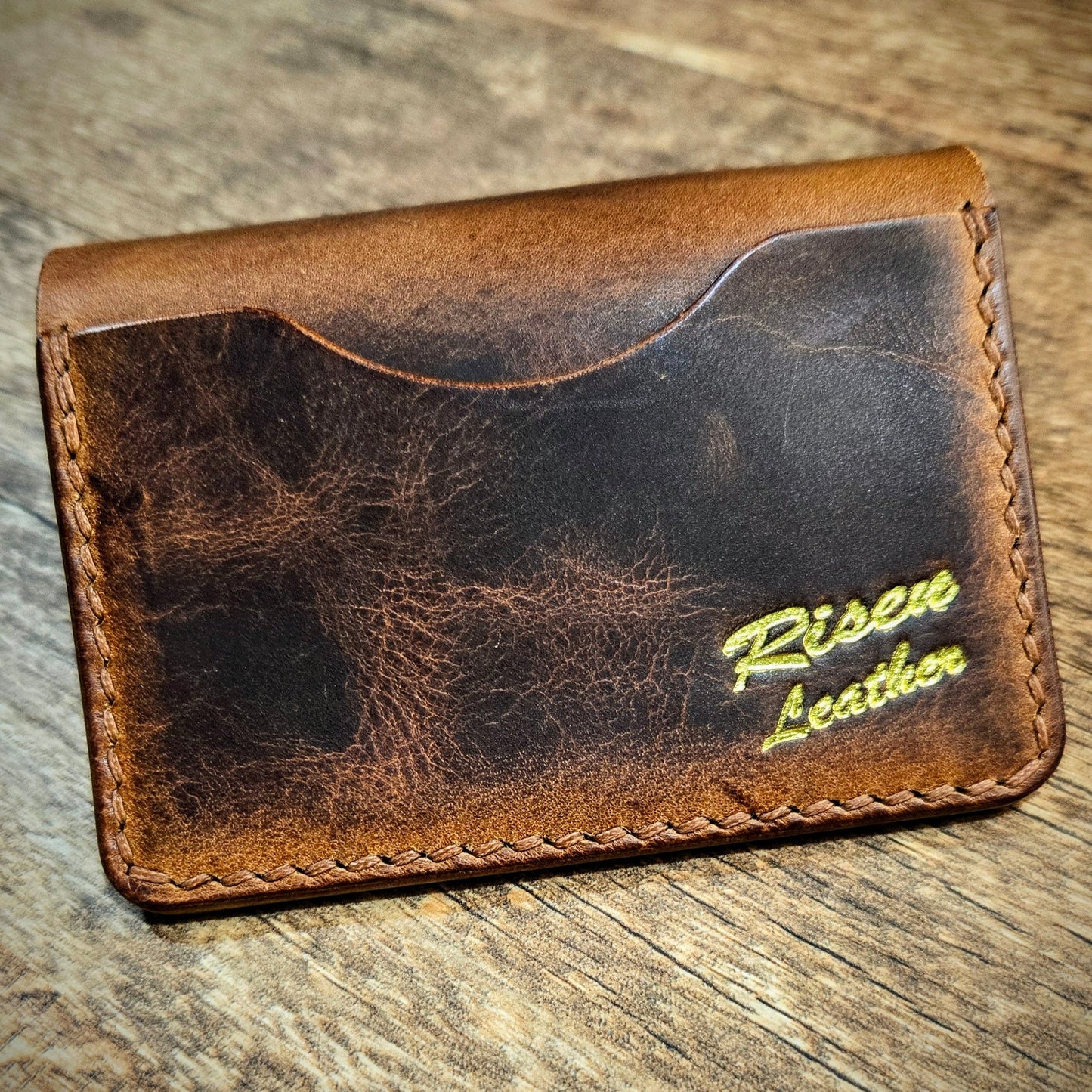 Brown leather wallet with 'Risen Leather' branding on a wooden surface
