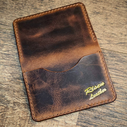 Brown leather wallet with 'Risen Leather' branding on a wooden surface