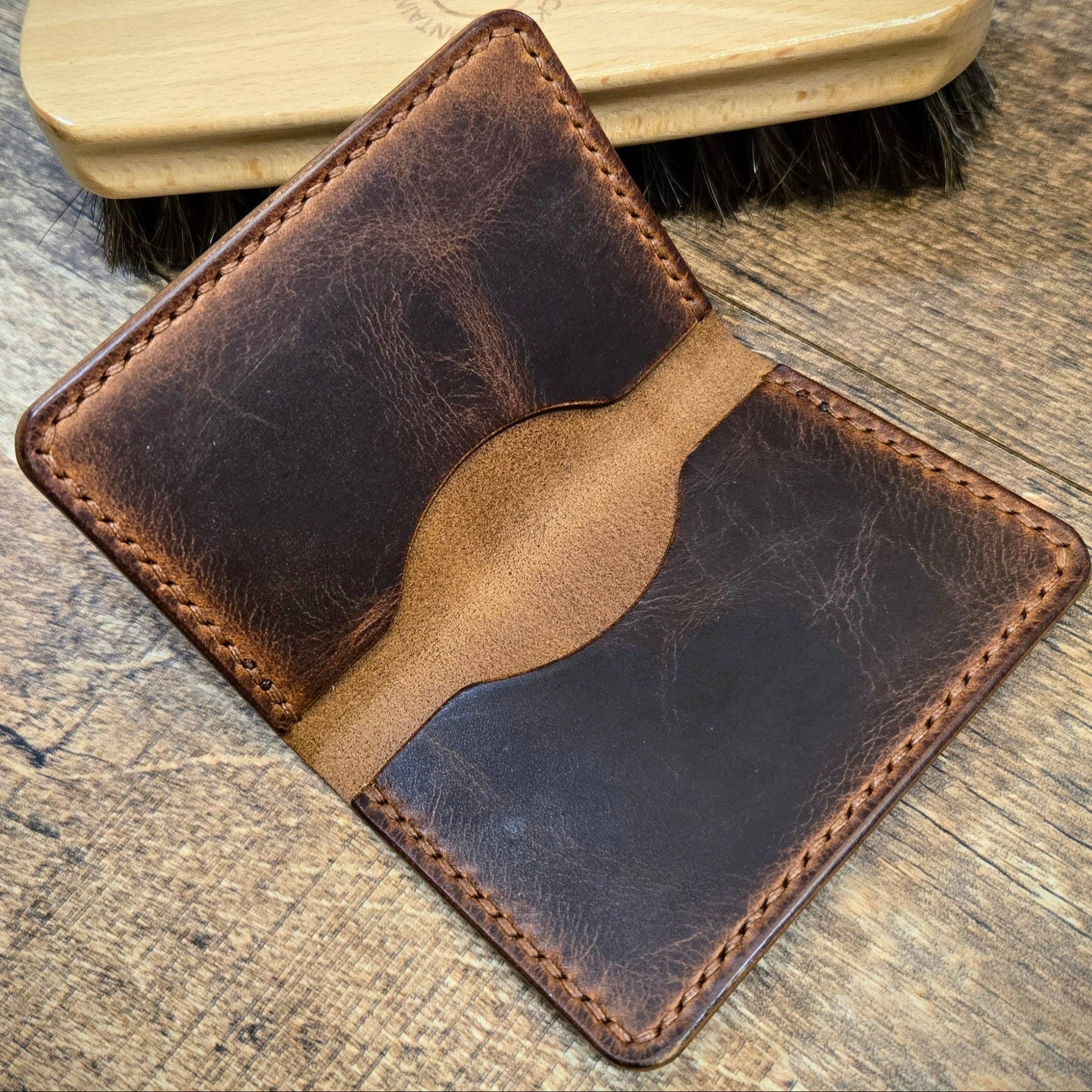 Brown leather wallet and wooden brush on a wooden surface