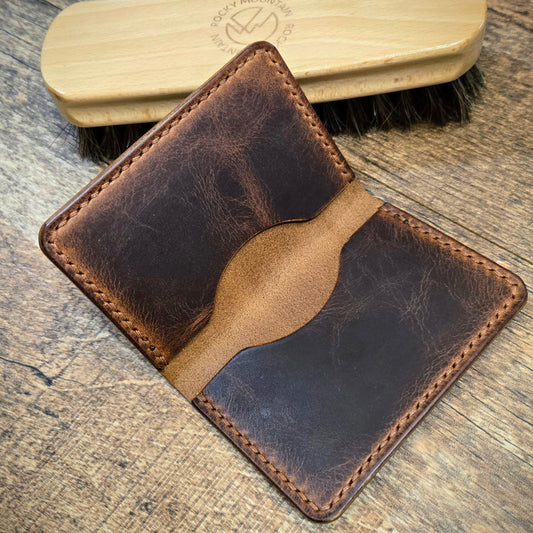 Brown leather wallet and wooden brush on a wooden surface