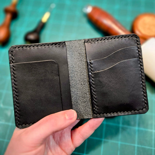 Black leather wallet held by a hand on a green cutting mat with tools in the background